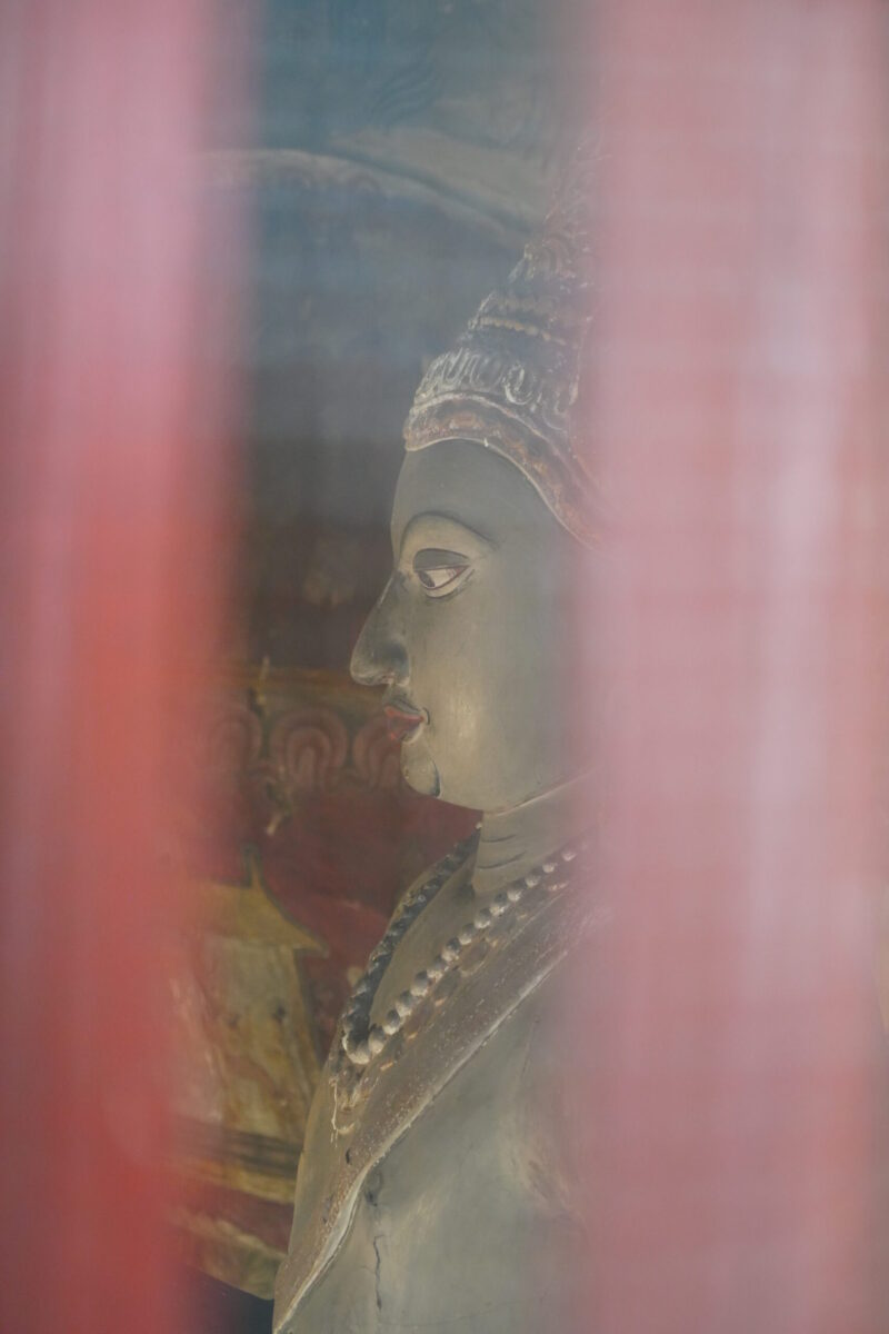 赤い柱越しに見える横顔の仏像彫刻